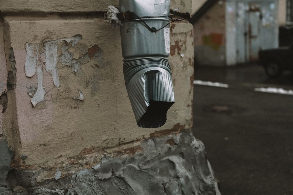 A downspout elbow connecting a seamless gutter run to a vertical drainage pipe along a home's corner