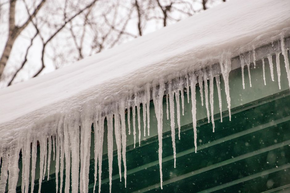 Icicles and a visible ice dam forming along a roof edge and gutter during winter